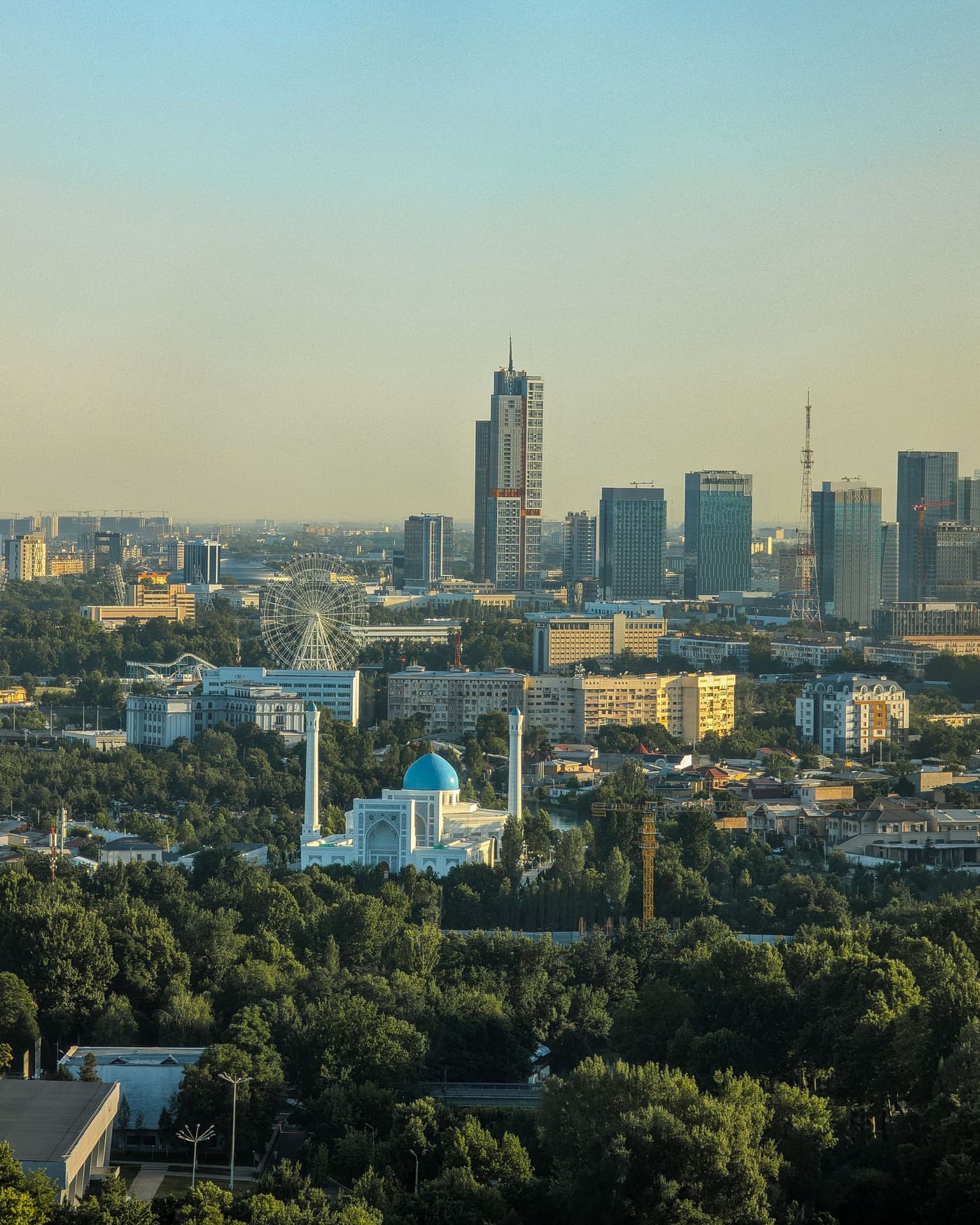 Daytime aerial view of Tashkent with green neighbourhoods, a blue-domed mosque, and the modern city skyline